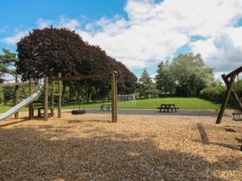 A playground with swings and slide near a grassy field with soccer goals and benches at Owl in Shobdon