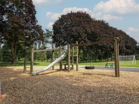 A playground with a slide and tire swing surrounded by trees and a bench near a soccer goal in a park at Owl in Shobdon