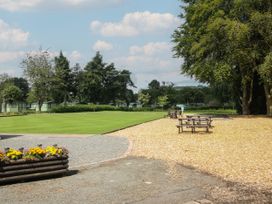 An outdoor area with picnic tables wood chip ground a green lawn flower bed trees and small cabins at Owl in Shobdon