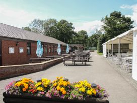 An outdoor seating area with wooden picnic tables umbrellas flower planter and white canopy tent at Owl in Shobdon