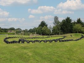 An outdoor play area with a track made of tires and wooden climbing structures on grass at Owl in Shobdon