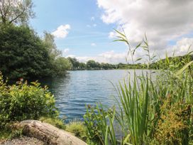 A lake surrounded by green plants and trees under a blue sky at Owl in Shobdon