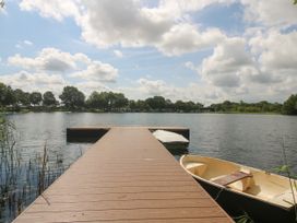 A wooden dock extending into a lake with a small boat tied to the side and trees around the shoreline at Owl in Shobdon