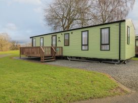 A green mobile home with a wooden deck on a grassy area at Owl in Shobdon