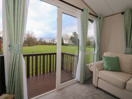A living room with glass sliding doors opening to a wooden balcony and green fields at Owl in Shobdon