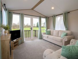 A living room with a sofa armchair television and glass doors with curtains at Owl in Shobdon
