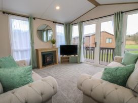 A living room with two beige sofas and green pillows a TV on a stand a fireplace and a round mirror on the wall at Owl in Shobdon