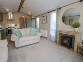 A living room with beige sofas green cushions a fireplace mirror and kitchen area at Owl in Shobdon