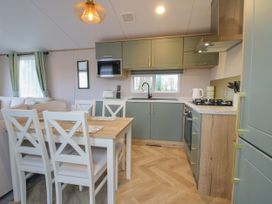 A kitchen and dining area with green cabinets a gas stove a microwave a dining table with four chairs and a sofa in the background at Owl in Shobdon