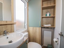 A bathroom with a white sink a toilet a frosted window wooden cupboards and shelves with toiletries and towels at Owl in Shobdon