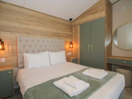 A bedroom with a bed with white linens and green throw with towels on it beside green wardrobe and dressing table with round mirror at Owl in Shobdon