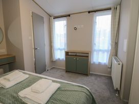 A bedroom with a bed covered with green bedding and folded towels two windows with curtains and a cabinet below them at Owl in Shobdon