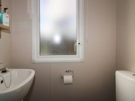 A bathroom with a sink and soap dispensers on a wooden shelf a frosted window a toilet paper holder with toilet paper and a toilet at Owl in Shobdon