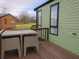 An outdoor deck with a table and chairs next to a green mobile home at Owl in Shobdon