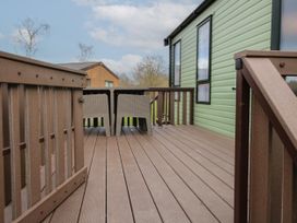 A wooden deck with two chairs and a table beside a green building at Owl in Shobdon