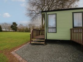 A green mobile home with wooden steps and railings on a gravel area next to a grassy field at Owl in Shobdon