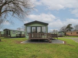 A green static caravan with a wooden porch surrounded by grass and other caravans at Owl in Shobdon
