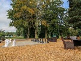 An outdoor area with a large chess set on a checkered board and wicker chairs under trees at Owl in Shobdon
