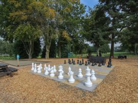 An outdoor area with a large chessboard and chess pieces surrounded by trees and wooden benches at Owl in Shobdon