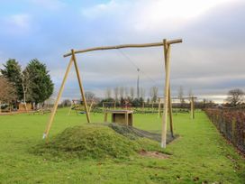 A playground with a zip line and swings on a grassy field at Owl in Shobdon