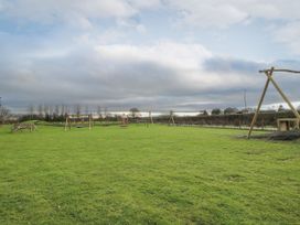 A large grassy field with playground equipment and wooden structures at Owl in Shobdon