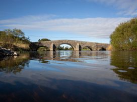 A bridge over water with trees and a blue sky at Felin Gogoyan Tregaron