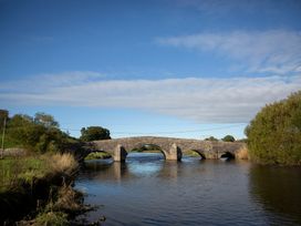 A bridge over water with trees and grass nearby at Felin Gogoyan Tregaron