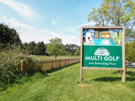 An outdoor sign for Multi Golf and Swimming Pool near trees and a wooden fence at Hazell Thorne Hideaway in Fritton