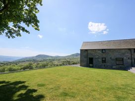 A stone house with a grassy yard and hills in the background at Ysgubor Maen Y Bardd Rowen near Conwy