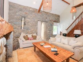 A living room with beige sofas a wooden coffee table stone walls and wooden stairs at Ysgubor Maen Y Bardd Rowen near Conwy