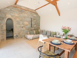 A dining area with a wooden table set with plates and glasses next to a lounge area with a sofa and cushions in a room with stone wall and wooden beams at Ysgubor Maen Y Bardd in Rowen near Conwy