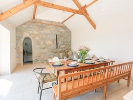 A dining area with a wooden table set with plates and glasses wooden benches chairs a stone wall and exposed wooden beams at Ysgubor Maen Y Bardd in Rowen near Conwy