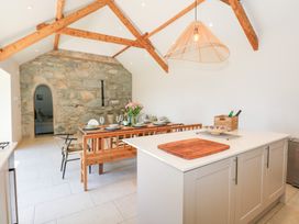 A kitchen and dining area with a stone wall wooden beams a dining table with place settings and a kitchen island with a cutting board at Ysgubor Maen Y Bardd in Rowen near Conwy