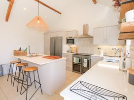 A kitchen with an island and three stools a refrigerator an oven a microwave and wooden beams on the ceiling at Ysgubor Maen Y Bardd Rowen near Conwy