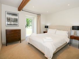 A bedroom with a double bed white bedding two bedside tables with lamps a chest of drawers and a door to the outside at Ysgubor Maen Y Bardd in Rowen near Conwy