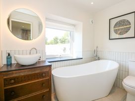 A bathroom with a freestanding bathtub a wooden vanity with a sink a round mirror a window and framed artwork at Ysgubor Maen Y Bardd in Rowen near Conwy