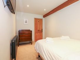 A bedroom with a bed covered in white linens and folded towels a wooden chest of drawers a wooden door and a mounted television at Ysgubor Maen Y Bardd in Rowen near Conwy