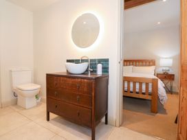 A bathroom with a toilet and wooden vanity with a vessel sink and round illuminated mirror next to a bedroom with a bed and bedside table at Ysgubor Maen Y Bardd in Rowen near Conwy