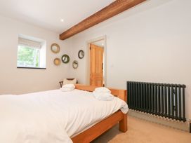 A bedroom with a wooden bed and white linens next to a black radiator and a window at Ysgubor Maen Y Bardd in Rowen near Conwy