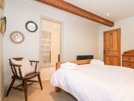 A bedroom with a wooden bed dressed in white linens and towels a wooden chair with a cushion wooden dresser wooden door and bathroom door at Ysgubor Maen Y Bardd in Rowen near Conwy