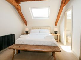 A bedroom with a bed with white linens wooden bench bedside tables lamps and visible bathroom at Ysgubor Maen Y Bardd Rowen near Conwy