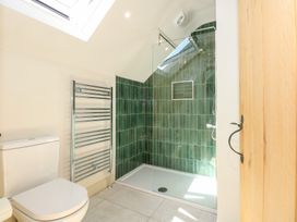 A bathroom with a toilet a chrome towel radiator and a shower with green tiled walls at Ysgubor Maen Y Bardd in Rowen near Conwy