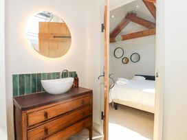 A bathroom sink with oval mirror and green tile backsplash next to a bedroom with a bed and round wall mirrors at Ysgubor Maen Y Bardd in Rowen near Conwy