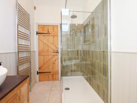 A bathroom with a wooden door a walk-in shower with green tiles and a chrome towel radiator at Ysgubor Maen Y Bardd Rowen near Conwy