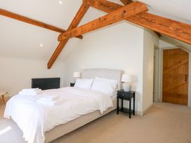 A bedroom with a bed with white bedding bedside tables with lamps wooden beams on the ceiling and a wooden door at Ysgubor Maen Y Bardd in Rowen near Conwy