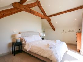 A bedroom with a bed with white linens bedside tables with lamps wooden exposed beams and a chest of drawers at Ysgubor Maen Y Bardd in Rowen near Conwy