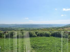 A landscape view of green fields forest and hills taken from behind a glass balcony at Ysgubor Maen Y Bardd in Rowen near Conwy