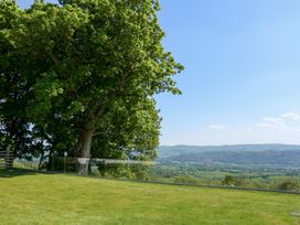 A grassy lawn with a large tree and a glass fence overlooking hills and fields at Ysgubor Maen Y Bardd in Rowen near Conwy