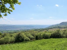 A landscape view of green fields and hills with trees under a blue sky at Ysgubor Maen Y Bardd in Rowen near Conwy