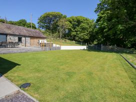 A large grassy yard with a stone building patio furniture a hot tub trees and a gate at Ysgubor Maen Y Bardd Rowen near Conwy